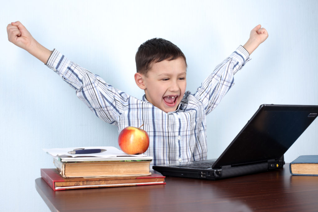 Boy at laptop throwing hands up in the air excited about the benefits of homeschooling
