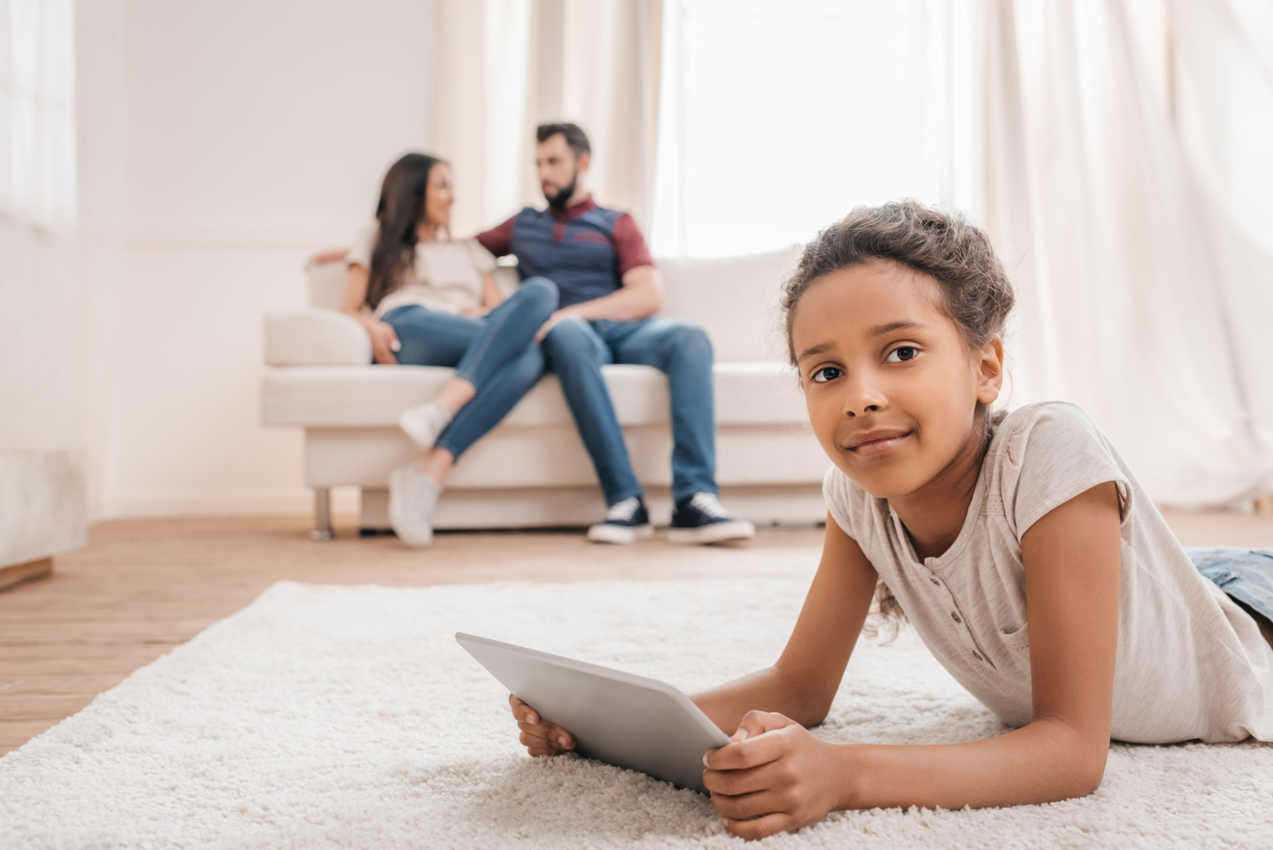 Image of child on a tablet while parents in the background discuss homeschool styles and methods