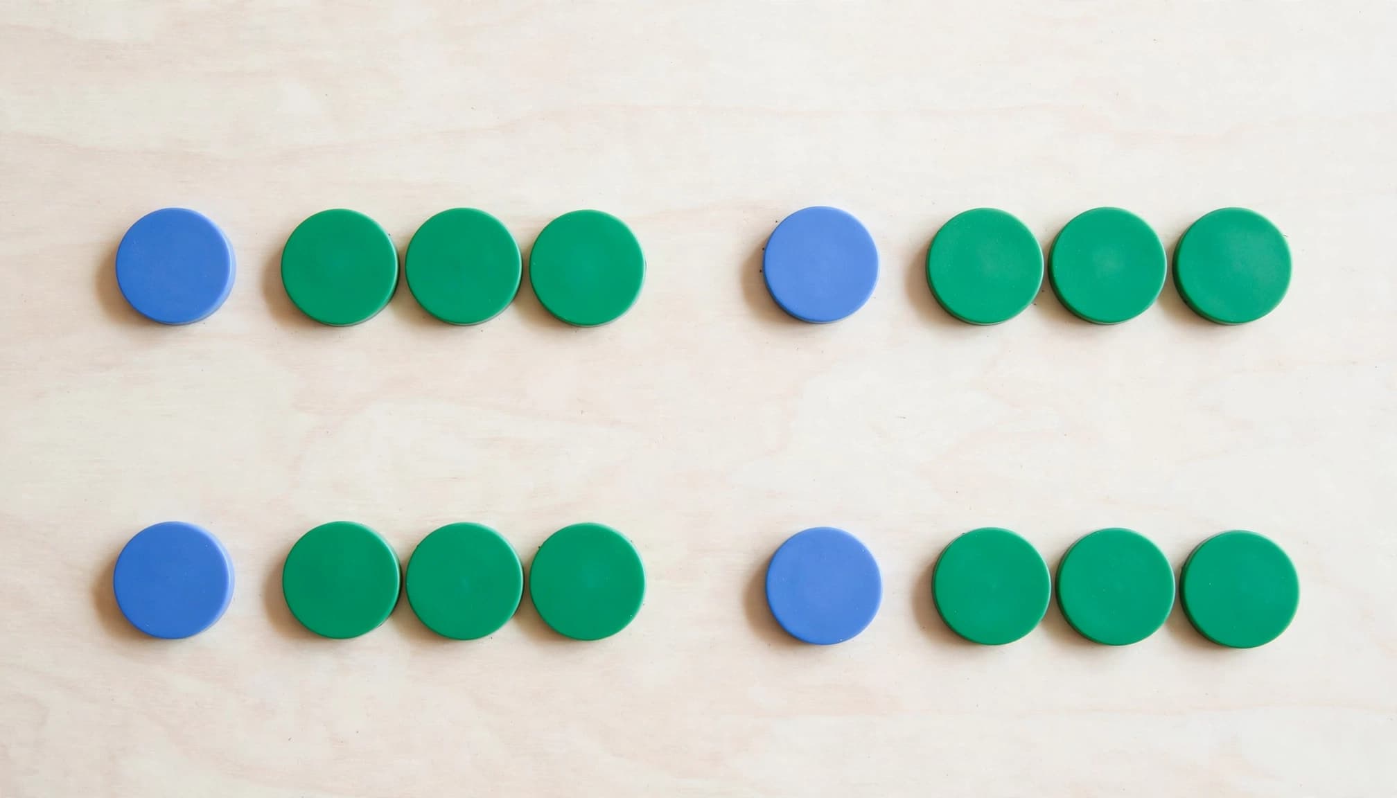 An overhead view of blue and green counters arranged in groups on a pale table.